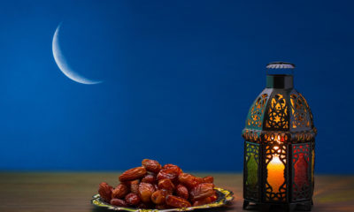 Picture of dates and Ramadan lamp against a silhouette of a sliver of the moon.