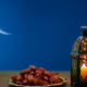 Picture of dates and Ramadan lamp against a silhouette of a sliver of the moon.