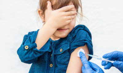 A photo of a young girl covering her eyes while receiving a shot.