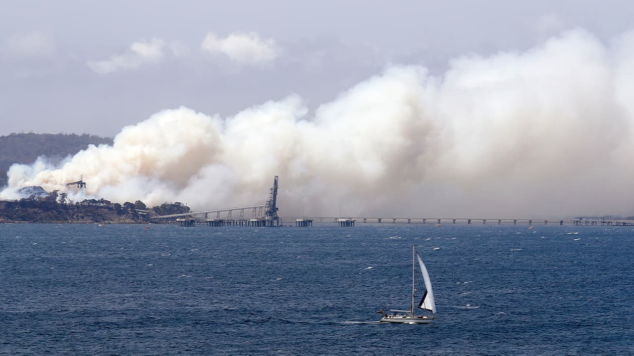 Photo of yacht sailing past a burning woodchip mill